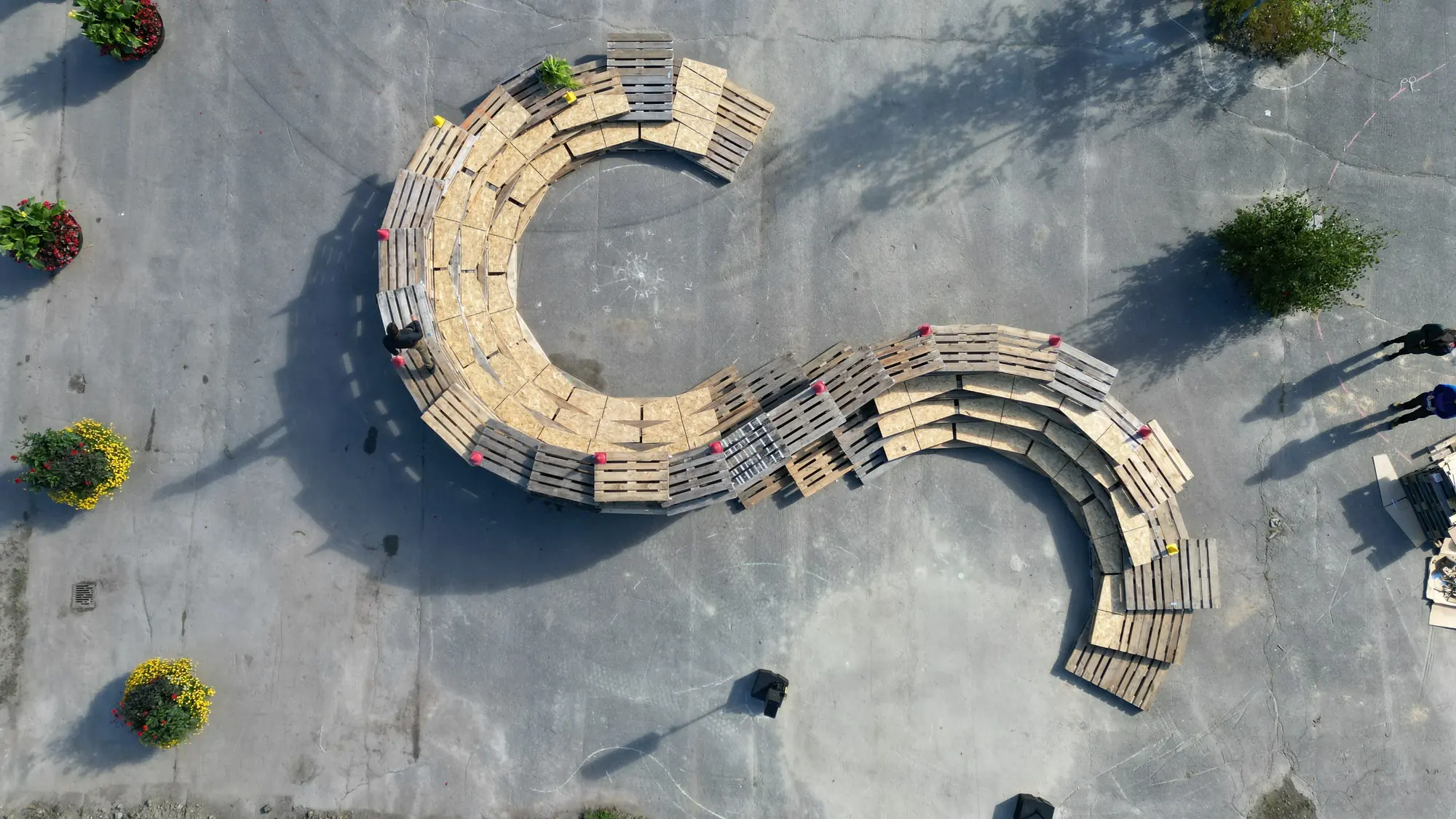 Aerial view of curving rows of stacked pallets forming an amphitheatre on asphalt