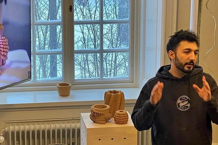 Raffaele talking students through printed clay tests, in a black hoodie, a snowy window and the printed pieces behind him