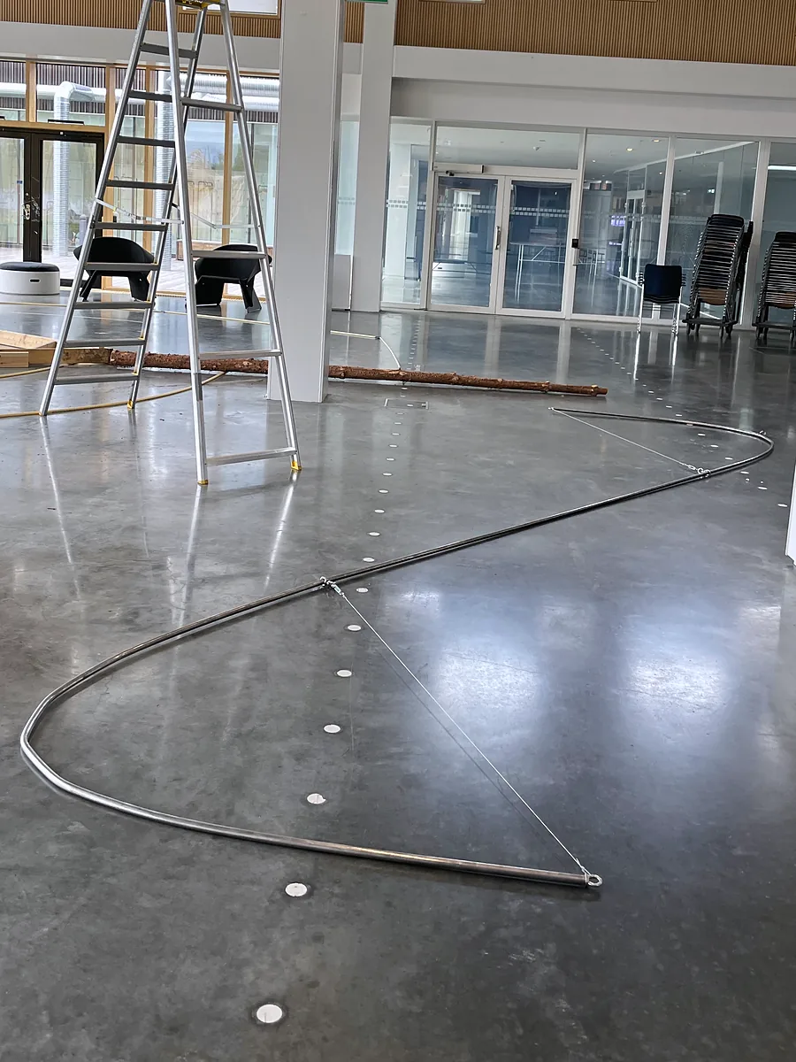 A long steel tube bent into a large S, laid on the concrete floor of the school hall