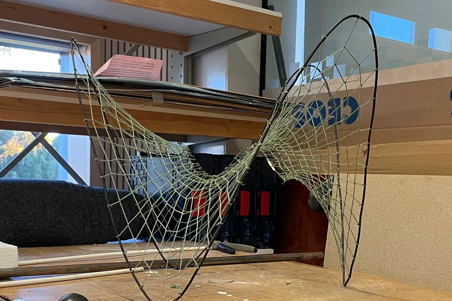 A rope net stretched between bent steel rods on a workbench
