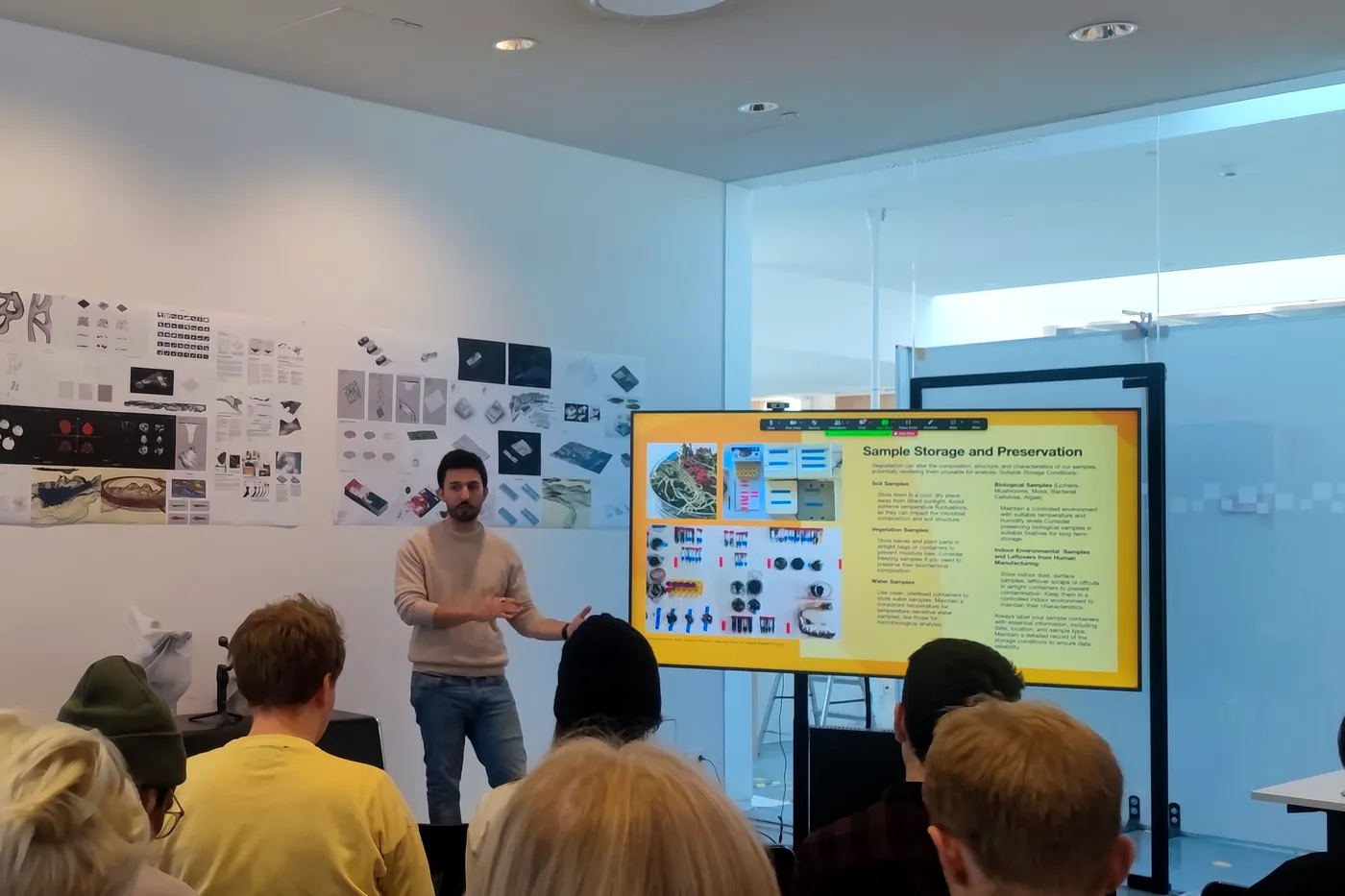 Raffaele giving a lecture to the studio, students seen from behind, a slide on sample storage and preservation beside him