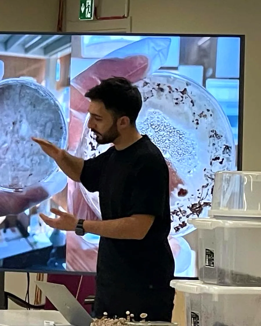 Raffaele lecturing in Studio 12 in front of a projected petri dish of mycelium, with samples on the table